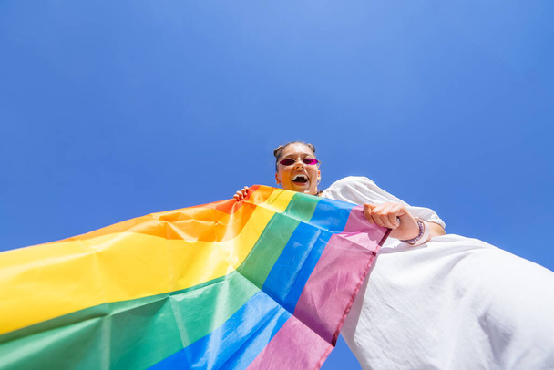 Nuori nainen kehittää sateenkaaren lipun taivasta vasten tukemaan LGBT-yhteisöä. - Valokuva, kuva