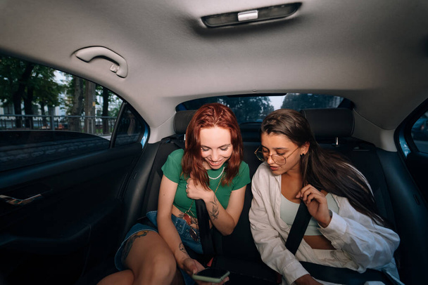 Vida real de amigos juntos en el asiento trasero de un taxi sosteniendo teléfonos celulares y revisando mensajes. - Foto, Imagen