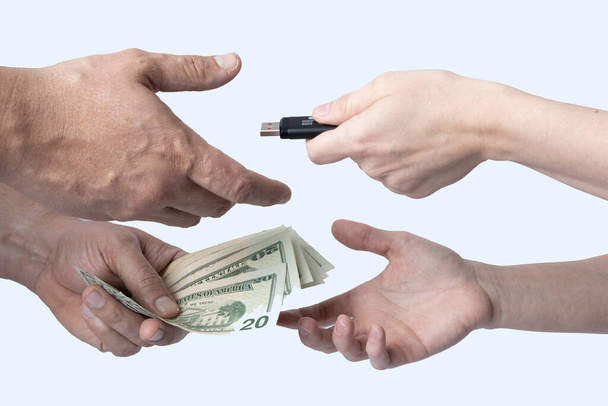 Cambiar un dispositivo de almacenamiento por dinero en efectivo entre dos individuos donde solo sus manos y antebrazos son visibles sobre un fondo blanco. - Foto, imagen