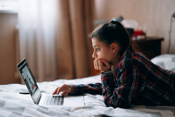 Επιλεκτική εστίαση της νεαρής γυναίκας εργασία, ενώ με φορητό υπολογιστή που βρίσκεται στο κρεβάτι - Φωτογραφία, εικόνα