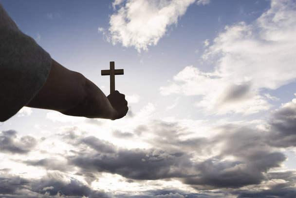 Emberi kéz tartja a keresztet az égen. a hit szimbóluma Isten imádsága. Megszabadulás. Imádkozom. Keresztény fogalom. - Fotó, kép