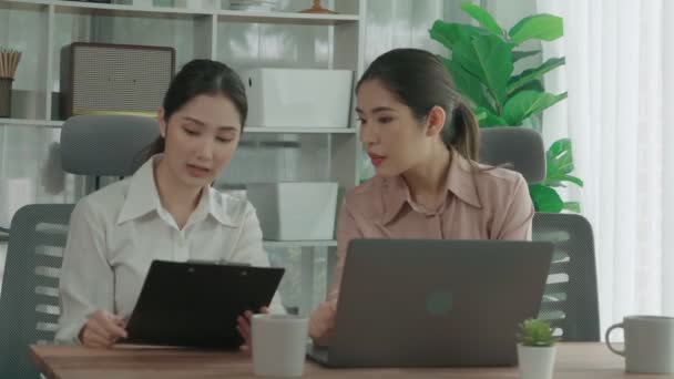 Two young enthusiastic businesswoman working together in the office workspace. Young colleagues having discussion and using laptop together. Modern office workers sitting together at desk. - Footage, Video