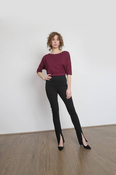 Serie de fotos de estudio de la joven modelo femenina con un traje cómodo simple, blusa de algodón orgánico de color burdeos y pantalones negros delgados con aberturas - Foto, Imagen