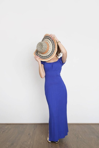 Uzun yaz mavi elbisesi ve geniş kenarlı hasır şapkasıyla genç bir kadın modelin stüdyo fotoğrafı.. - Fotoğraf, Görsel