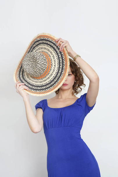 Studio photo of young female model in long summer royal blue dress and wide brim straw hat. - Photo, Image