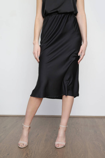 Γυναικείο μοντέλο με μαύρο καμιζόλα μεταξωτό μπλουζάκι και τυλιγμένη φούστα midi. Κομψό μονόχρωμο καλοκαιρινό ντύσιμο. Φωτογραφία στούντιο μόδας. - Φωτογραφία, εικόνα