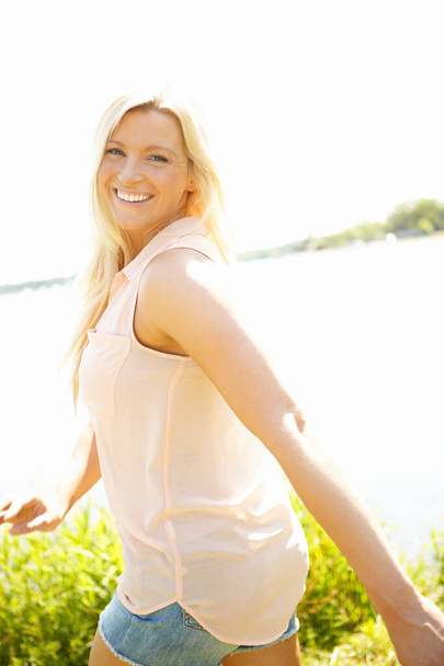 J'adore le plein air. Portrait d'une jeune femme blonde souriante marchant près d'un lac - Photo, image