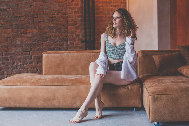 Beautiful glamorous elegant stylish woman with curly hair sitting on the brown sofa - Fotografie, Obrázek