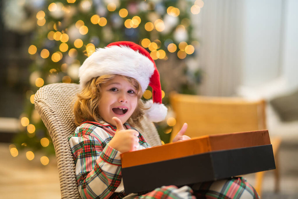 Surprise child opening Christmas magic presents. Little excited kid open with Christmas gift box, celebrating Christmas or New Year near Christmas tree at home - Fotó, kép