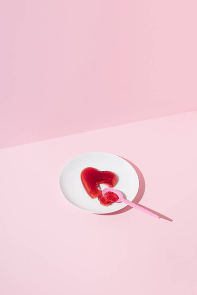 Coeur de gelée rouge ramassé avec une cuillère en plastique sur une plaque blanche. Amour ou Valentines concept minimal. - Photo, image