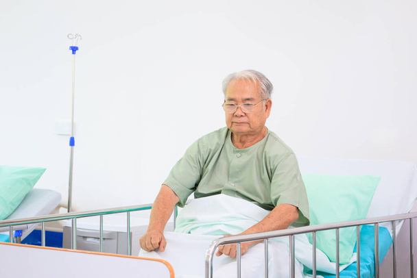 Elder Asian man in nursing home sitting on the bed alone. Lonely Asian old man sitting and vacant looking for something. Mental health care - mental wellbeing in elder people concept. - Foto, imagen