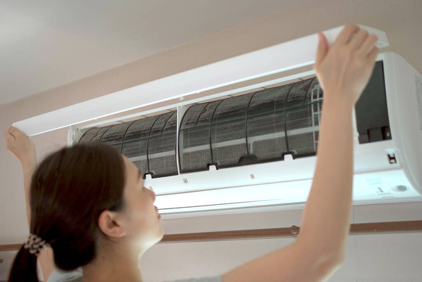 Asiática ama de llaves subiendo una escalera para limpiar un filtro de aire acondicionado en la habitación. - Foto, Imagen