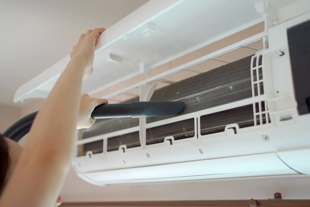 Hembra asiática ama de llaves subiendo una escalera para limpiar un filtro de aire acondicionado en el dormitorio. Mujer que utiliza la máquina de vacío para aspirar una partícula polvorienta en la ventilación del aire acondicionado o la bobina de enfriamiento. - Foto, Imagen