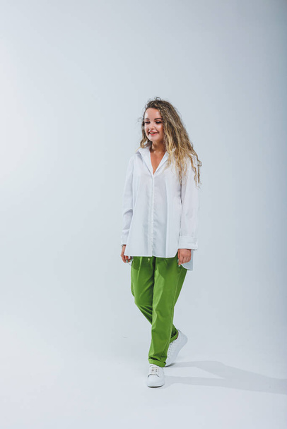 Young curly woman in a white cotton shirt and pants on a white background. Female mole - Fotó, kép
