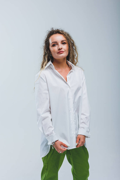 Young curly woman in a white cotton shirt and pants on a white background. Female mole - Foto, Imagem