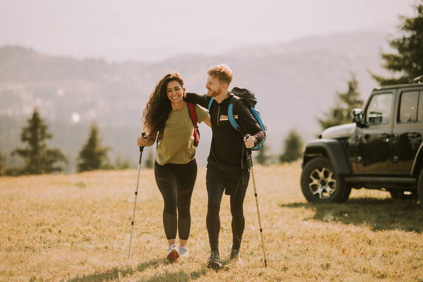 Usmívající se mladý pár začíná chodit s batohy přes zelené kopce - Fotografie, Obrázek