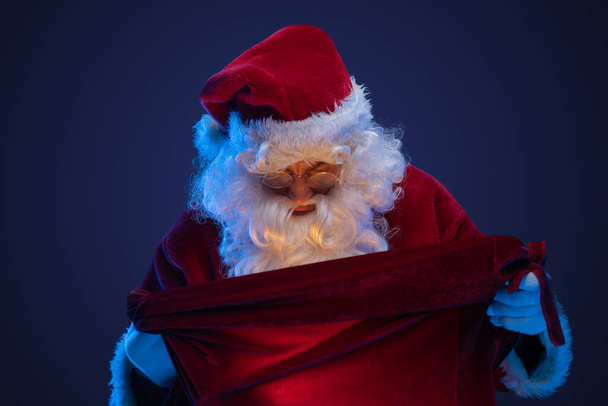 Prise de vue de Père Noël habillé en costume rouge regardant sac avec des cadeaux. - Photo, image