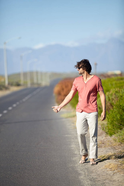 Azt hiszem, stoppolnom kell. Egy fiatalember stoppolni próbál, miközben egy elhagyatott úton sétál. - Fotó, kép