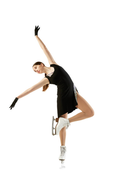Junges Teenie-Mädchen, Eiskunstläuferin in schwarzem Bühnenkostüm, vereinzelt vor weißem Hintergrund. Konzept der Fähigkeiten, Sport, Schönheit, Wintersport. Kopierraum für Werbung - Foto, Bild
