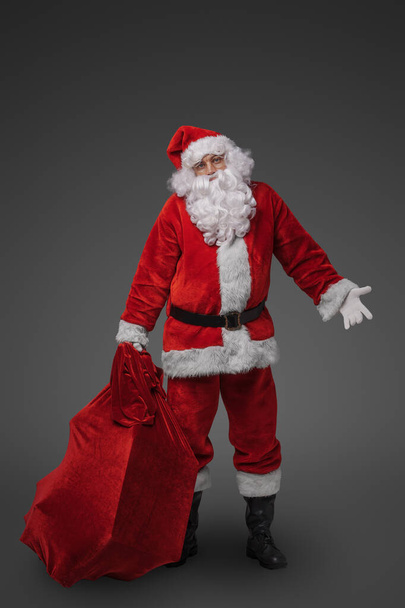 Photo of cheerful santa dressed in christmas red clothes against gray background. - Photo, Image