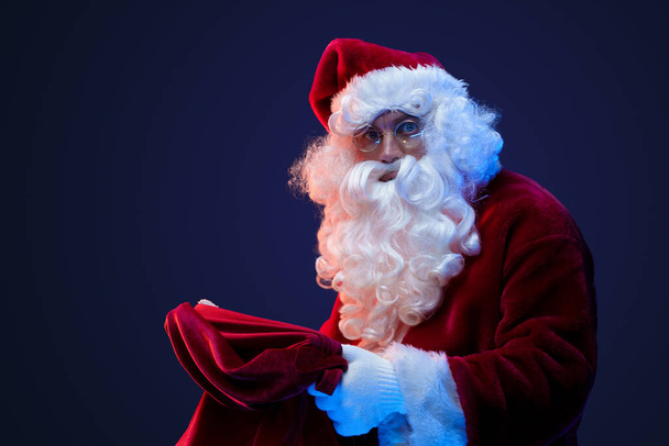 Portrait de Santa Claus barbu avec costume rouge et sac sur fond sombre. - Photo, image