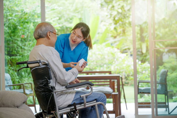 Asian young woman nurse pills with help prescribes medicine to older disabled patient on wheelchair when elderly senior man patients time to go home at nursing home care. Medicine and health care - Foto, Imagen