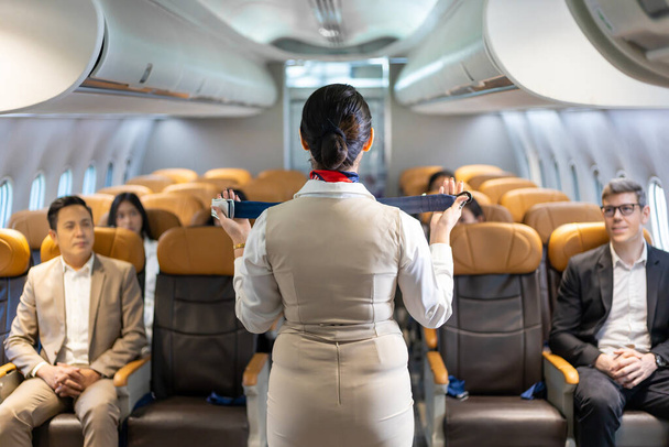 Aziatische stewardess demonstreert de veiligheidsprocedure met veiligheidsgordel voordat ze opstijgt in het vliegtuig voor cabine- en luchtvaartpersoneel - Foto, afbeelding