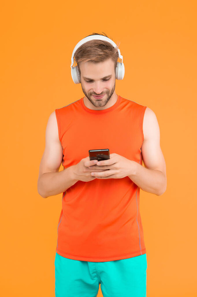 fröhlicher bärtiger Mann hört Musik in digitalen Kopfhörern per Handy-App in sportlicher Kleidung zum Training, soziales Netzwerk. - Foto, Bild