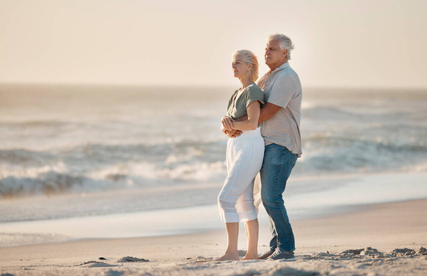 Reifer Ehemann umarmt seine Frau am Strand. Ein älteres Paar, das am Strand liebevoll ist. Ein älteres Ehepaar genießt die Aussicht auf das Meer. Reifes Paar im gemeinsamen Urlaub am Meer. - Foto, Bild