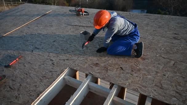 Carpenter hammering nail into OSB panel on the roof top of future cottage. Man worker building wooden frame house. Carpentry and construction concept. - Séquence, vidéo