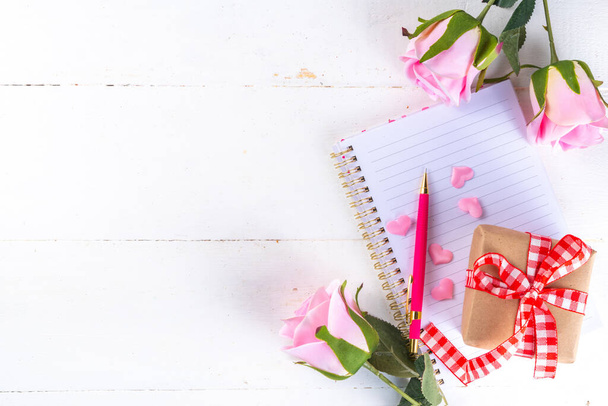 8 maart Dag van de Vrouw, Valentijnsdag wenskaart achtergrond met rozen bloemboeket, geschenkdoos met rood lint, hart vormen decor, op witte houten tafel bovenaanzicht kopieerruimte  - Foto, afbeelding