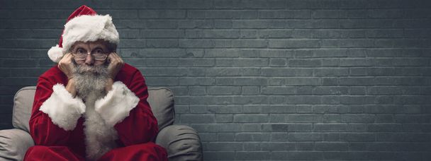 Santa Claus sitting on the armchair and waiting for Christmas, he is resting his head on his hands - Fotoğraf, Görsel