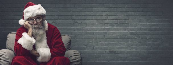 Lazy bored Santa Claus leaning on his hand and relaxing on the armchair, he is waiting for Christmas - Фото, зображення