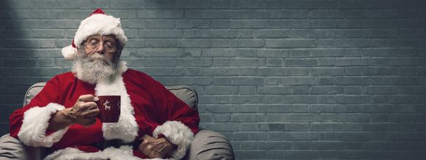 Santa Claus relaxing at home on the armchair and having an hot drink - Фото, зображення