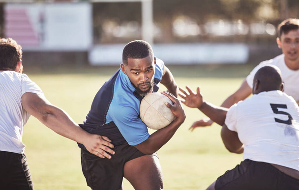 Jogador de rugby afro-americano fugindo de um adversário enquanto tenta marcar uma tentativa durante uma partida de rugby fora em um campo. Homem negro fazendo uma jogada para tentar ganhar o jogo para sua equipe. - Foto, Imagem