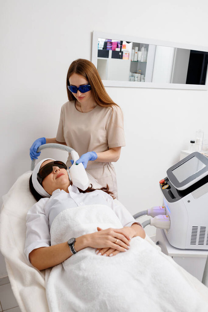 Profesyonel kozmetik uzmanı klinikte çürük yenileme cilt tedavisi yapıyor. Radyo dalgası kaldırma. Yüz gerdirme işlemi için güzellik uzmanının elinde ultrason cihazı - Fotoğraf, Görsel