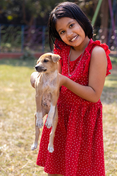Una bambina indiana gioca con un simpatico cucciolo marrone sul campo - Foto, immagini