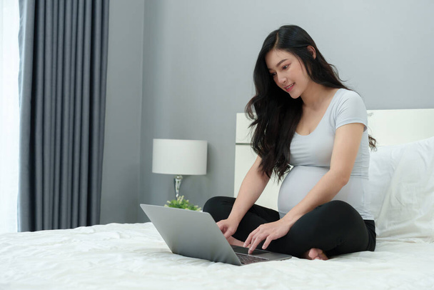 pregnant woman using laptop computer on a bed - Foto, Imagem