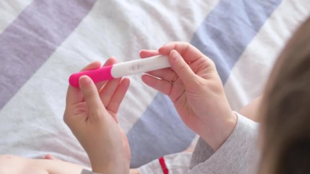 ベッドに横になって妊娠検査をする幸せな女性。2本の線で肯定的な妊娠テストを保持している認識できない女の子.妊娠の概念、家族計画. - 映像、動画