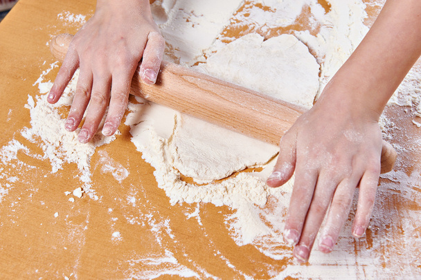 Girl prepare dough with rolling pin on kitchen table - Foto, afbeelding