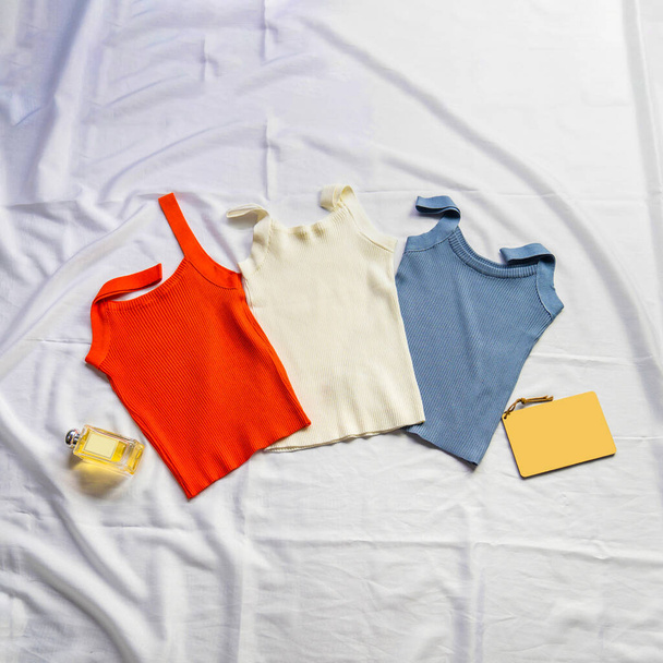 En la sábana blanca había tres camisetas cisterna, rojas, blancas y azules, intercaladas con perfume, modelo y portátil. - Foto, imagen