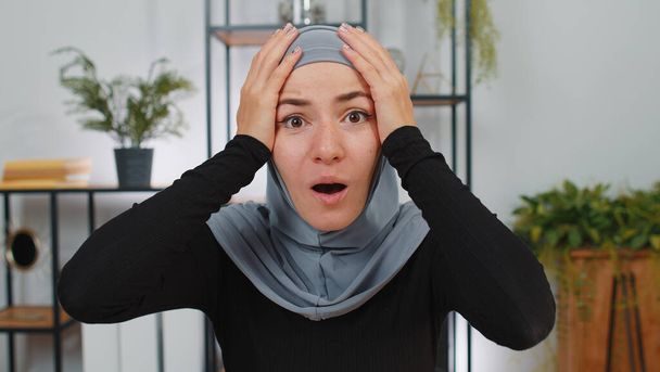 Oh, Dios mío, Wow. Emocionada joven mujer de negocios musulmana sorprendida vistiendo pañuelo de cabeza hijab mirando a la cámara con ojos grandes, conmocionada por la victoria repentina, buenas noticias de victoria, celebrando. Chica sorprendida en la oficina en casa - Foto, Imagen