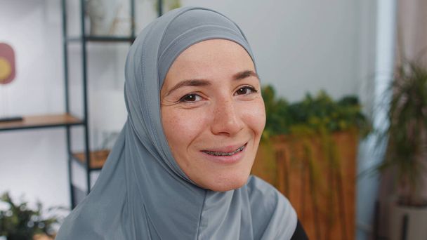 Портрет счастливой спокойной молодой мусульманской деловой женщины в хиджабе, улыбающейся дружелюбно, с приятным выражением лица, мечтательным отдыхом, релаксацией - приятная новость. Девушка в современном домашнем офисе - Фото, изображение