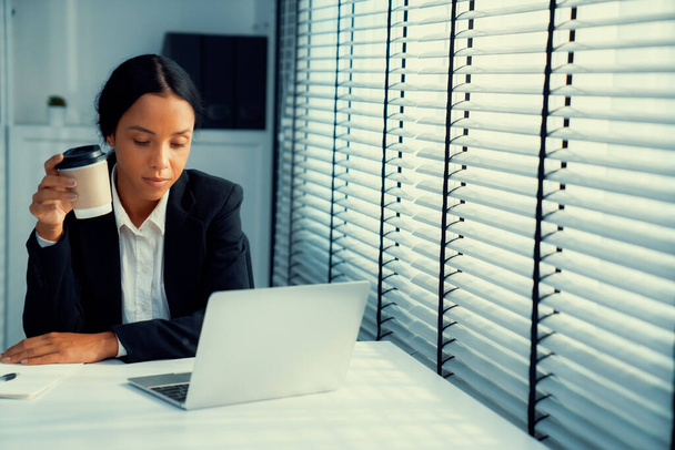Competent female employee sits at her desk with a cup of coffee. Modern employee working with a drink, recreation during working hours, caffeine for people who are working - Photo, Image