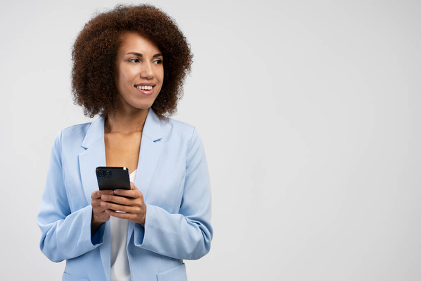 Gyönyörű mosolygós afro-amerikai nő gazdaság okostelefon segítségével mobil app vásárlás online elszigetelt a háttérben, másolás tér  - Fotó, kép