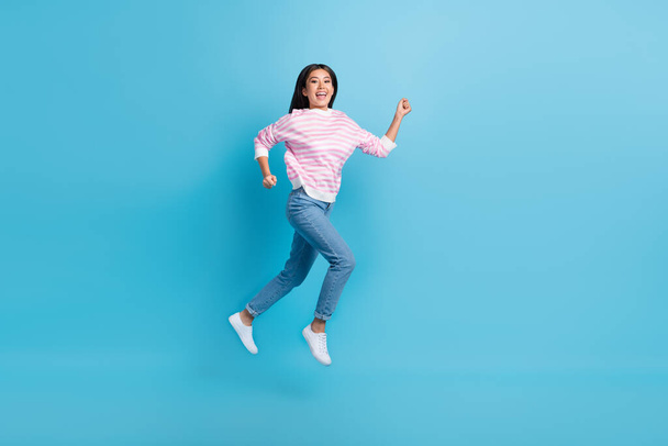 Full length photo of excited pretty girl dressed pink pullover jumping high running fast isolated blue color background. - Foto, afbeelding