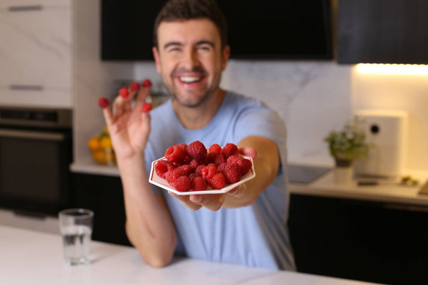 portrait of handsome young man with raspberries at kitchen - Foto, immagini