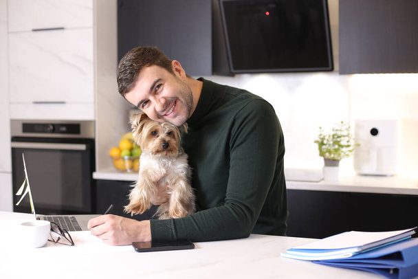 πορτρέτο του όμορφου νεαρού άνδρα με το χαριτωμένο σκυλάκι του στην κουζίνα - Φωτογραφία, εικόνα