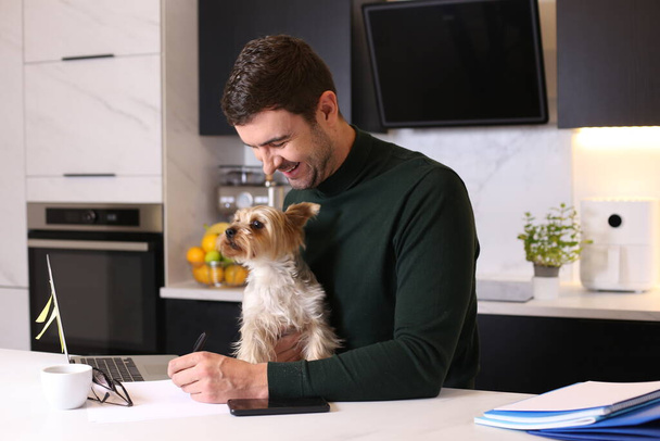 portrait of handsome young man with his cute little dog at kitchen - Фото, изображение