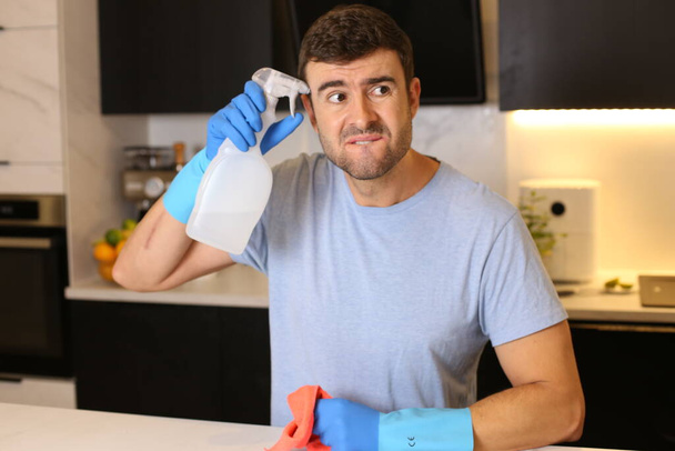 portrait of handsome young man with cleaning supplies at kitchen - Photo, Image